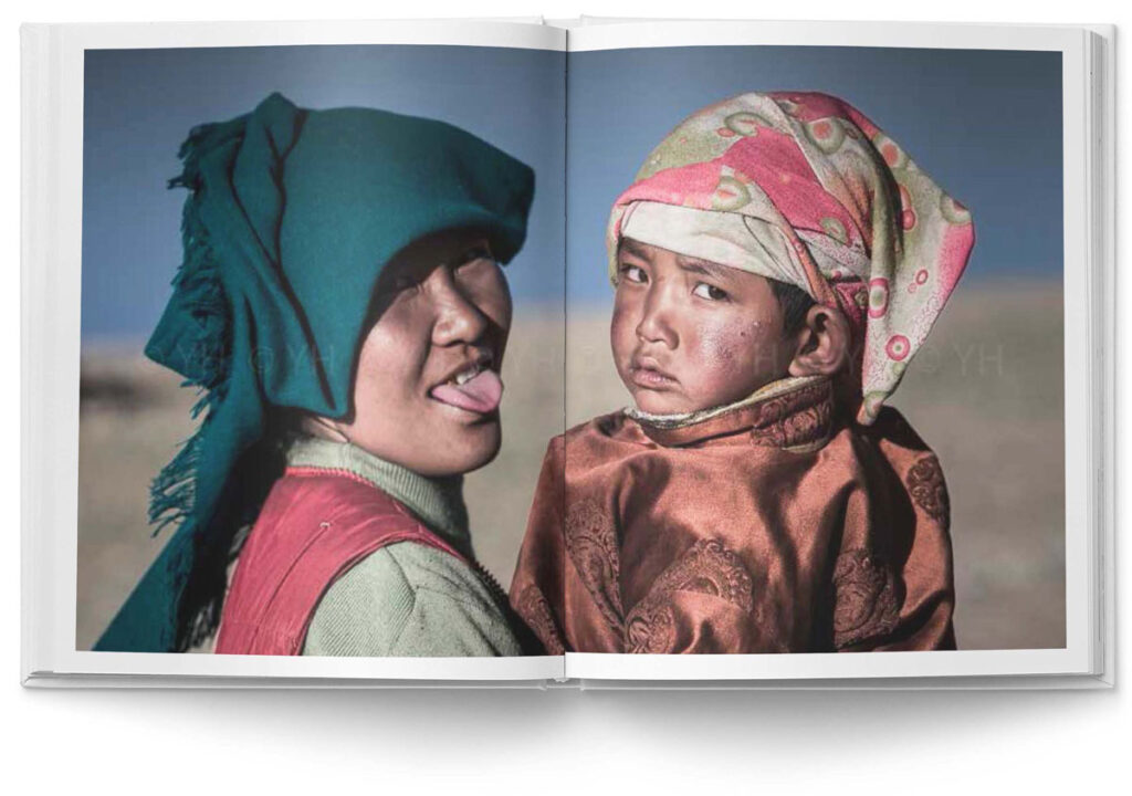 Buch ›100 Tage Tibet‹: Portraitaufnahme von einer Mutter mit Kind auf dem Arm in Tibet. Die Mutter streckt lachend dem Fotografen die Zunge heraus.